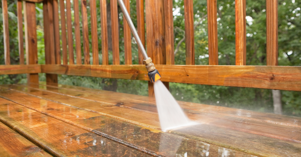A person is using a high pressure washer to clean a wooden deck.