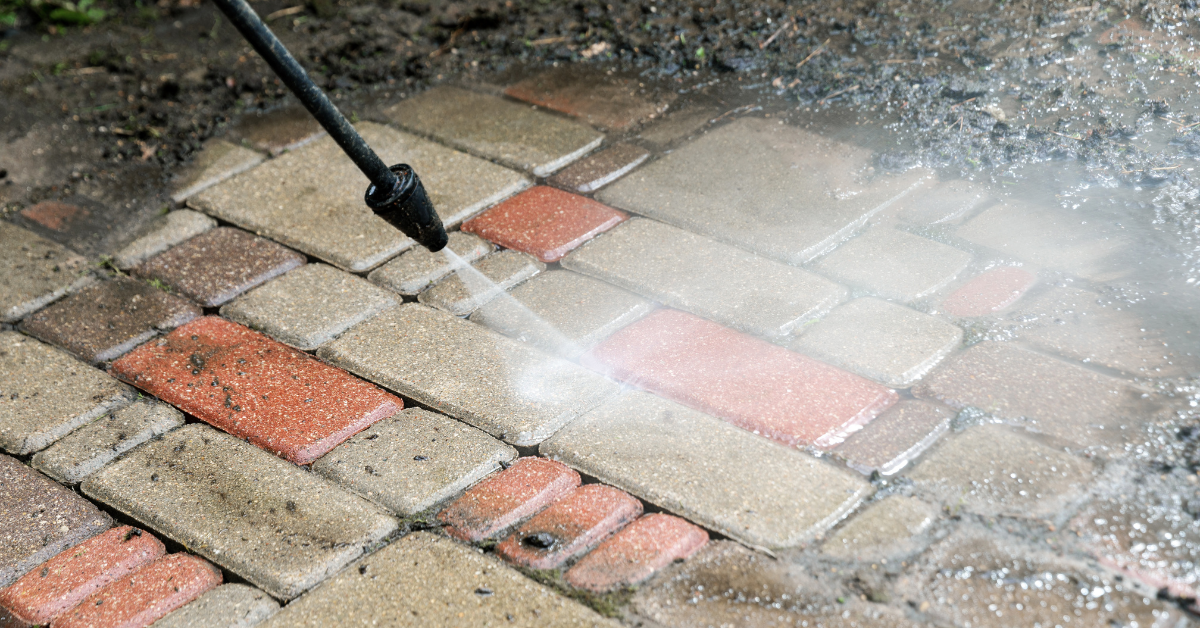 A person is using a high pressure washer to clean a brick walkway.